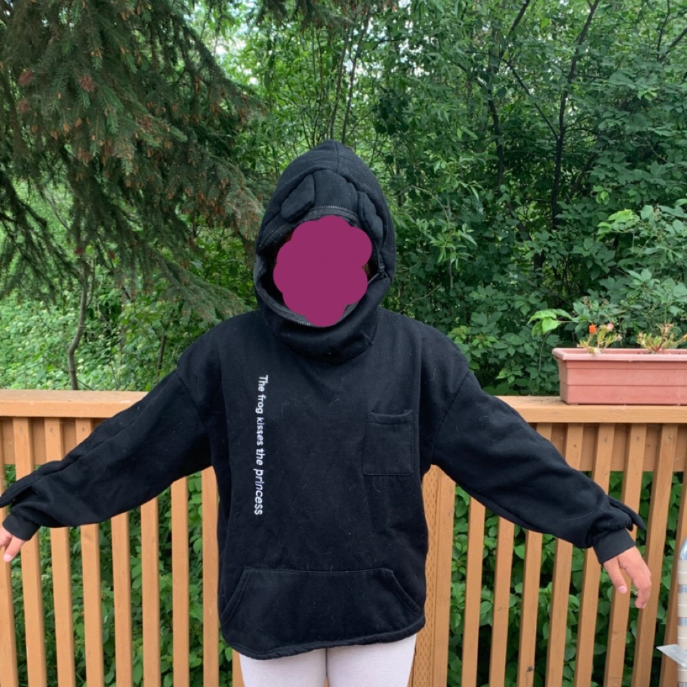 A frog hoodie that has the words “the frog kisses the princess” on it.